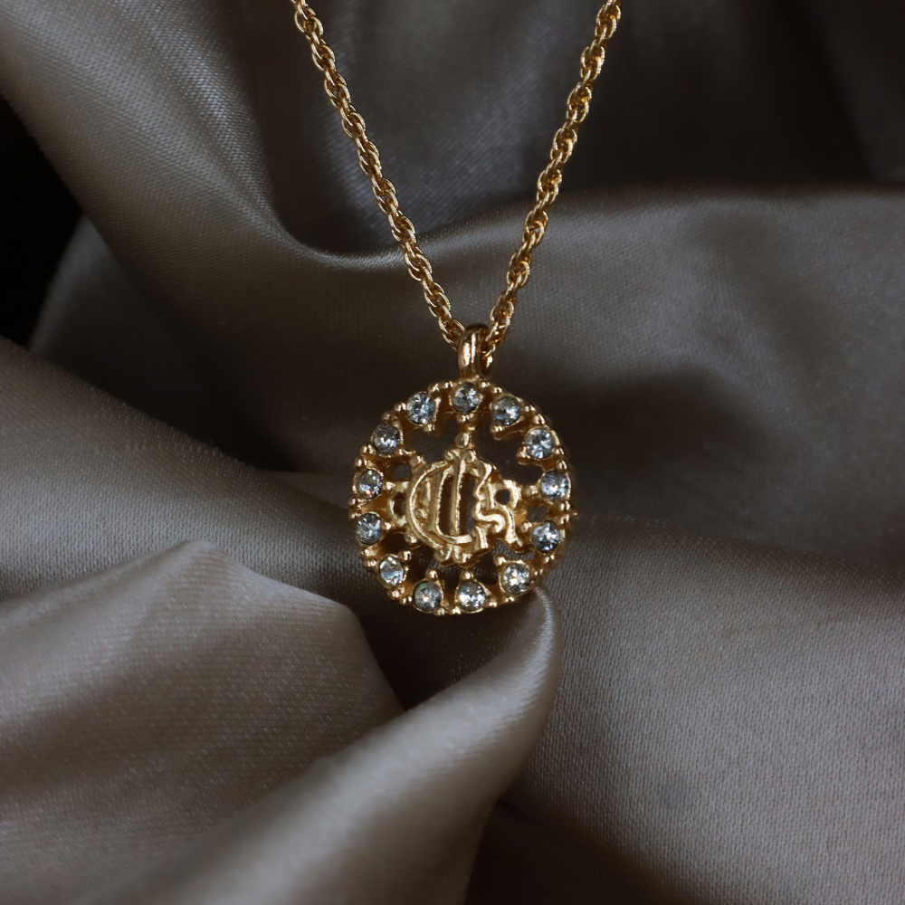 Christian Dior 金色 CD Logo 圓牌項鏈正面近照，展示鏤空字母與外圈透明石飾